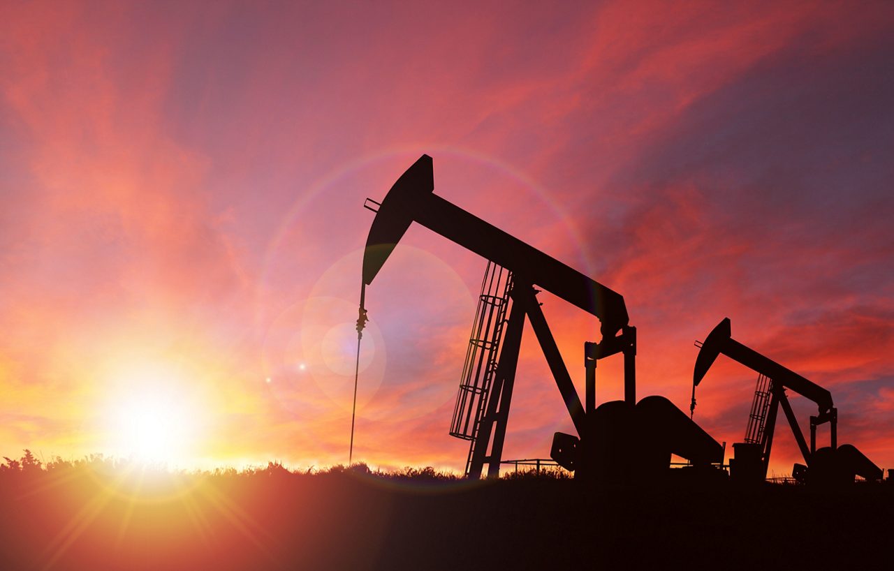 Pump jack silhouette against a sunset sky with deliberate lens flare and copy space 