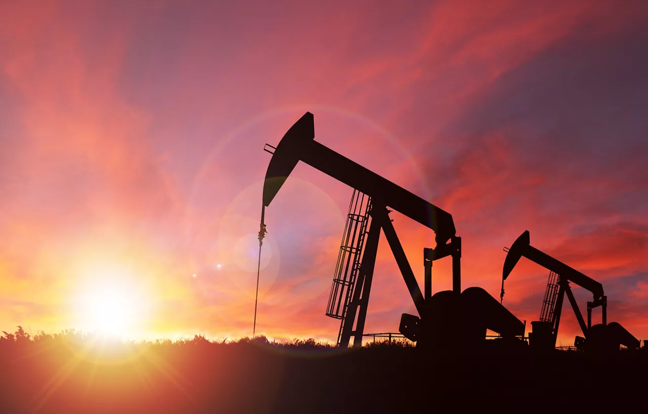 Pump jack silhouette against a sunset sky with deliberate lens flare and copy space.