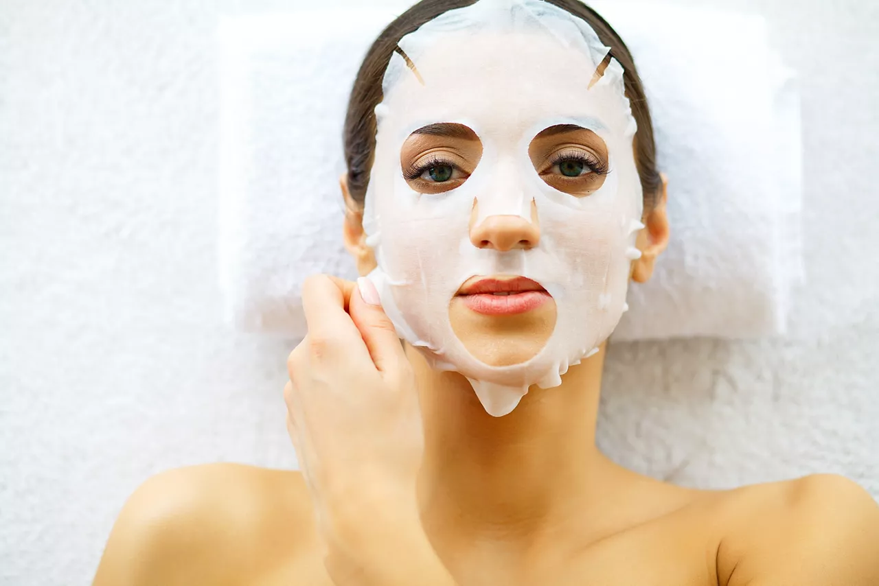 Woman lying down on white towels with skin care sheet mask on her face.