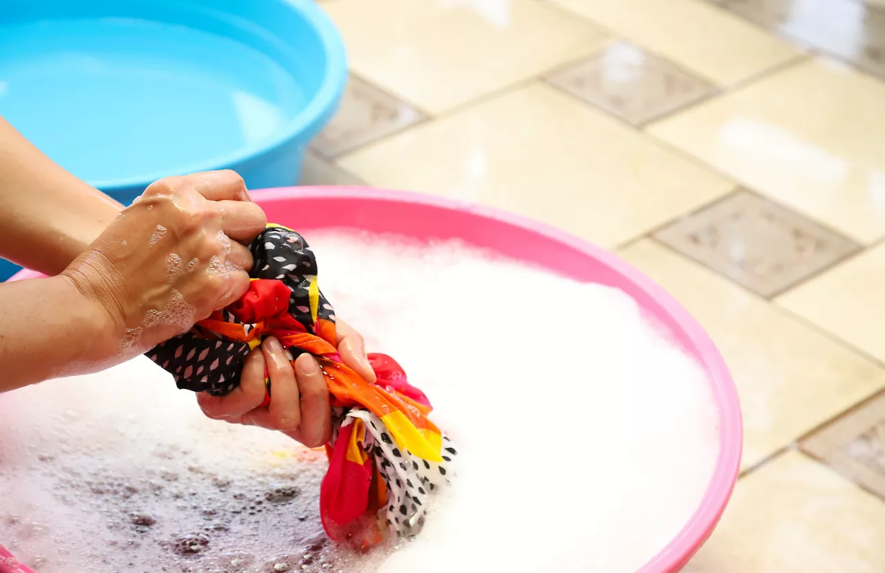 Closeup of outdoor colored clothes washing in plastic basin on the floor by woman's hands 