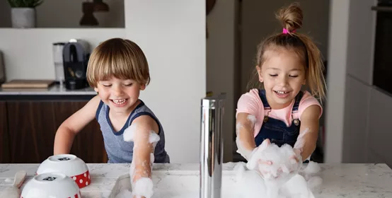 Kids playing with suds while washing dishes in a modern sink