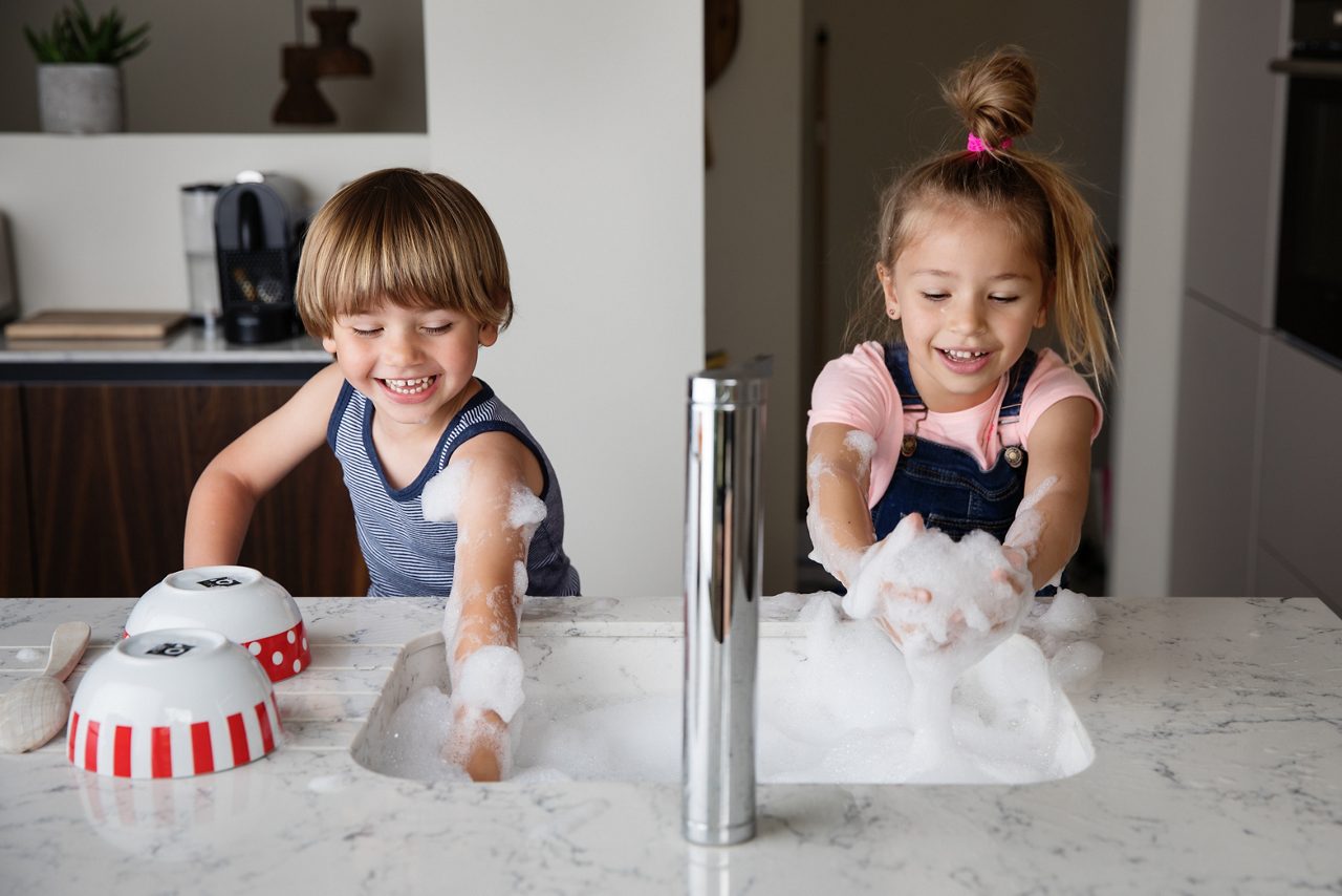 Kids playing with suds while washing dishes in a modern sink