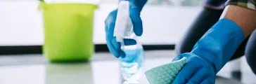 Man with blue rubber gloves cleaning a hard surface floor with a spray bottle  