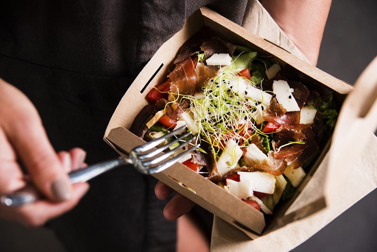 A person dipping fork into a salad inside a cardboard food box