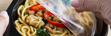Woman hands holding open cling wrap and take-out food in plastic boxes 