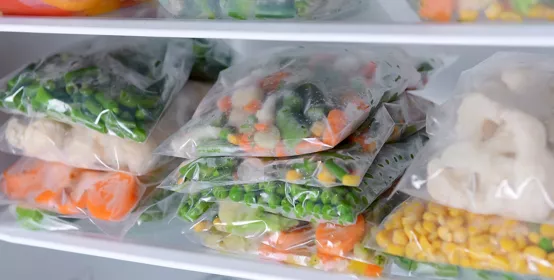 Plastic bags and containers with frozen vegetables in refrigerator