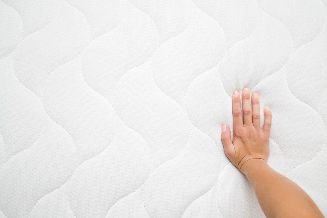 Woman's hand pressing on white mattress. Checking hardness and softness. Point of view shot. Copy space. Empty place for text or logo. Top view. Close up.