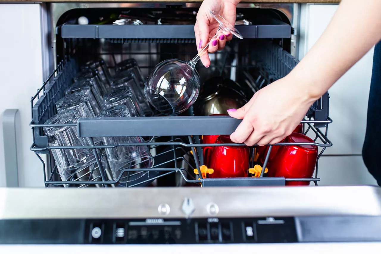Woman's hand with an open dishwasher filled with clean dishes