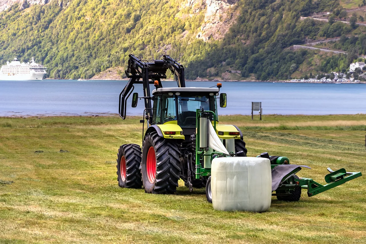 Small tractor with a round bale wrapper on a field in Geiranger, Norway.