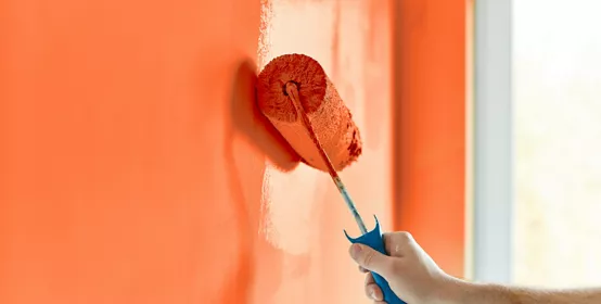 Male hand painting wall with paint roller. Renovating with red orange colorpaint 