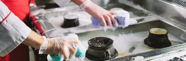 Restaurant workers cleaning stainless steel commercial stove