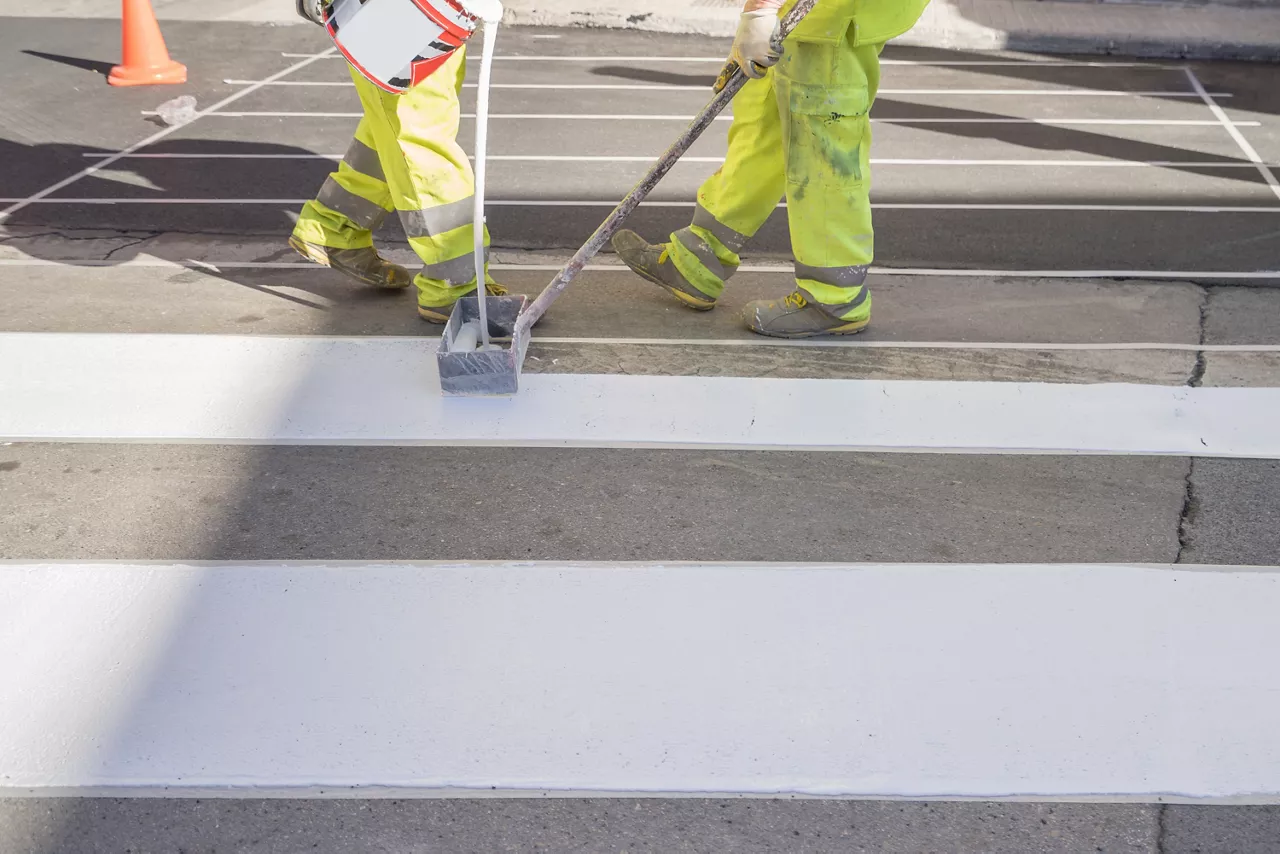 Workers painting white street lines on pedestrian crossing with screedbox