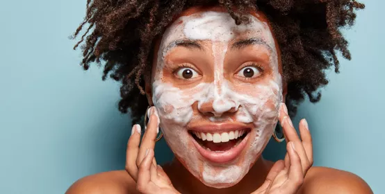 Happy lady wets face with foam.