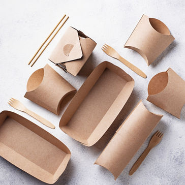 Recipientes de papelão para alimentos, como bandejas de papelão e caixas com utensílios em um balcão