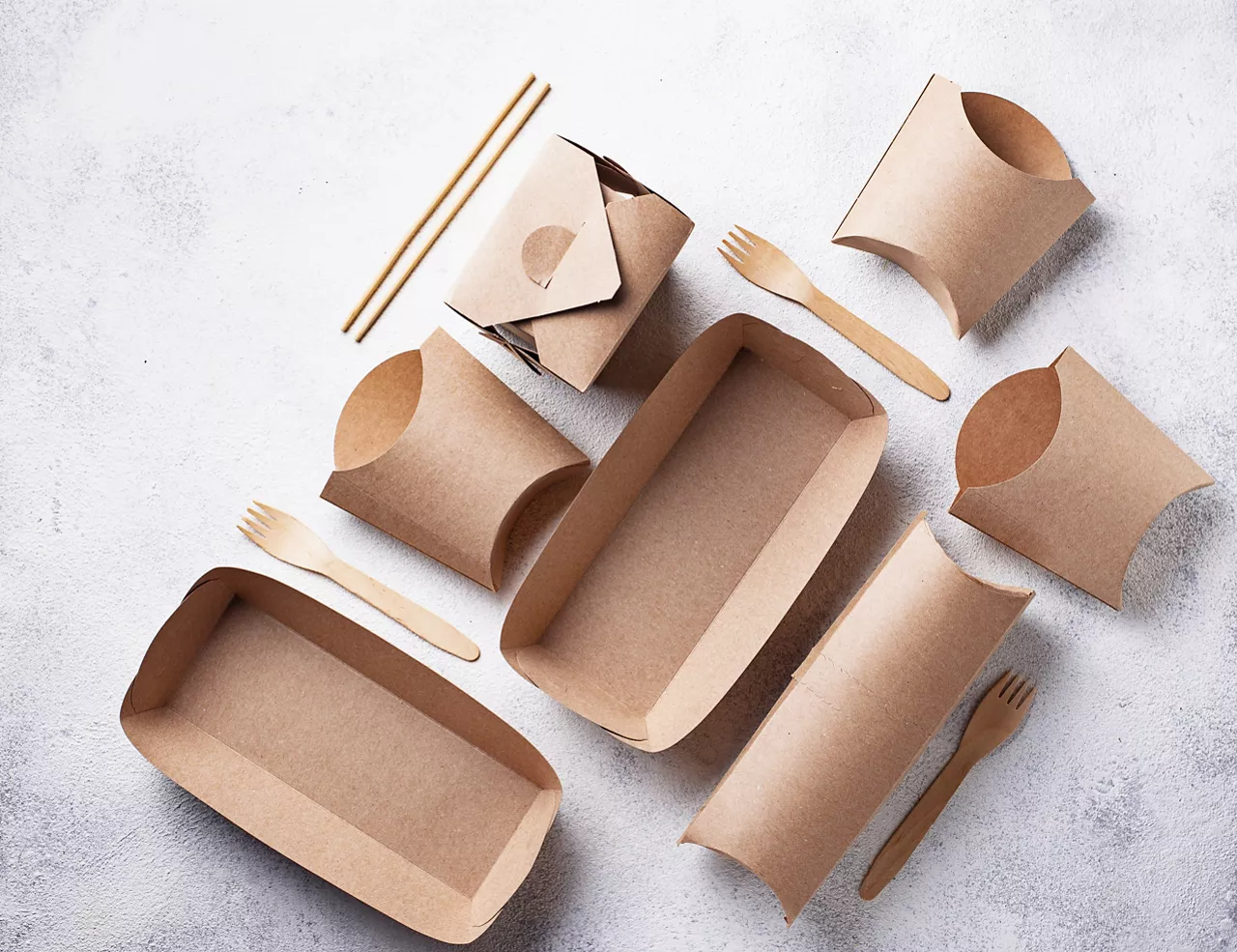 Cardboard food containers like cartons, trays and boxes with utensils displayed on a counter