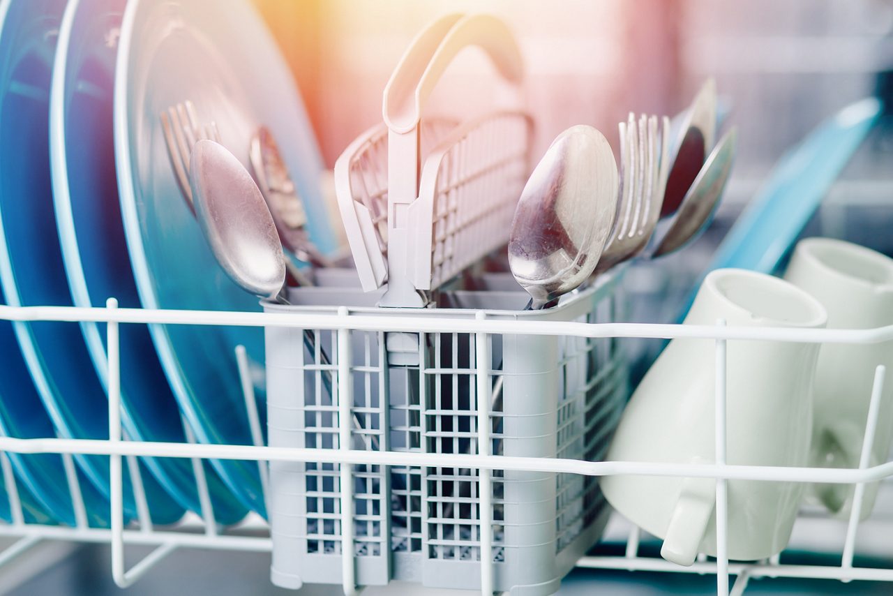 Open dishwasher with clean shine dishes and forks, spoons, cutlery. Concept water saving.