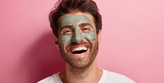 joyful delighted man has clay mask on face