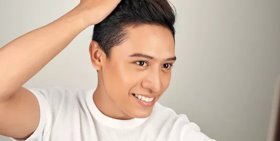 Happy handsome smiling Asian man touching his hair