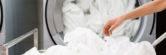 Cropped view of housemaid near white bed sheets in laundry.