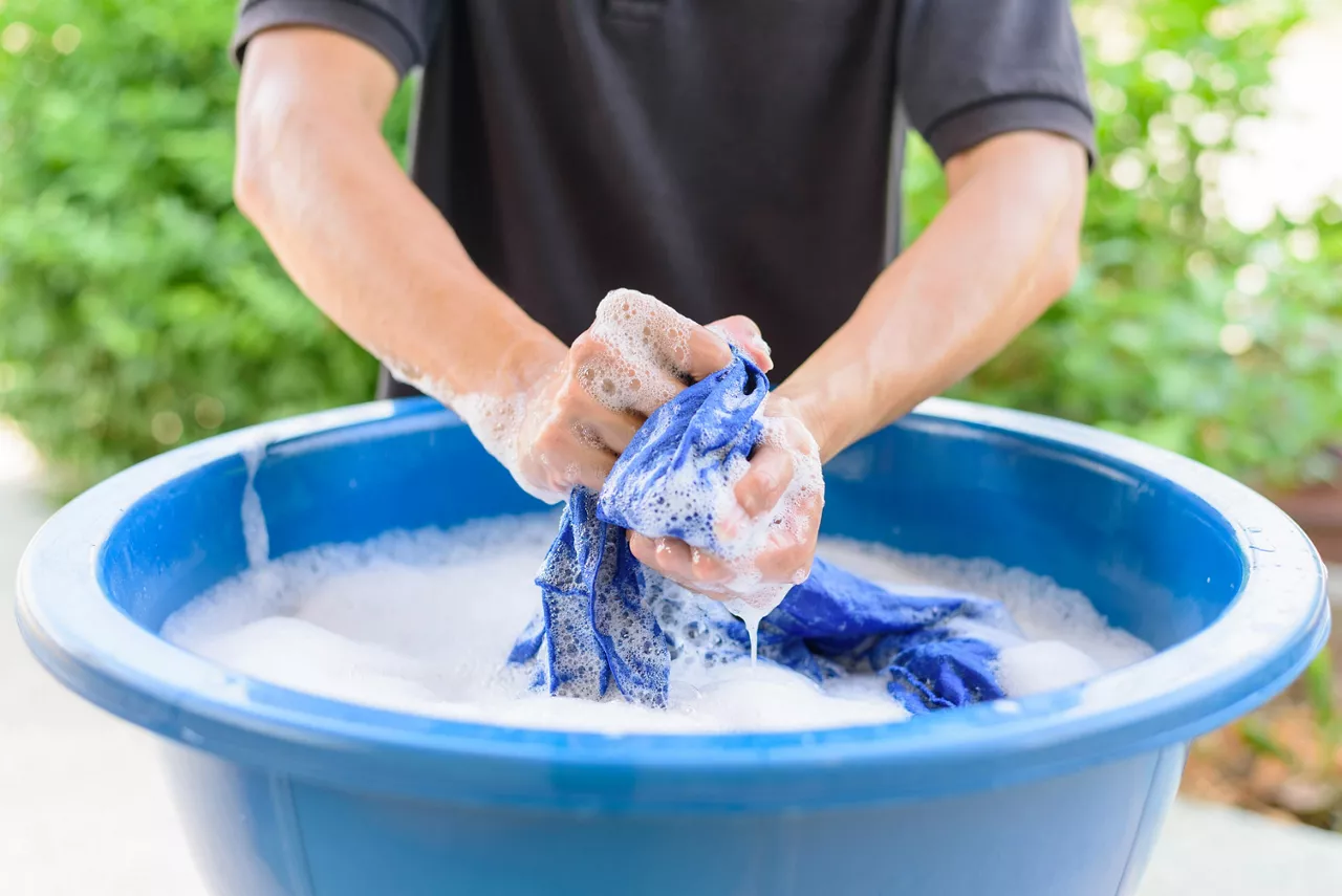 A man washing clothes by hand in a blue basin outdoors  