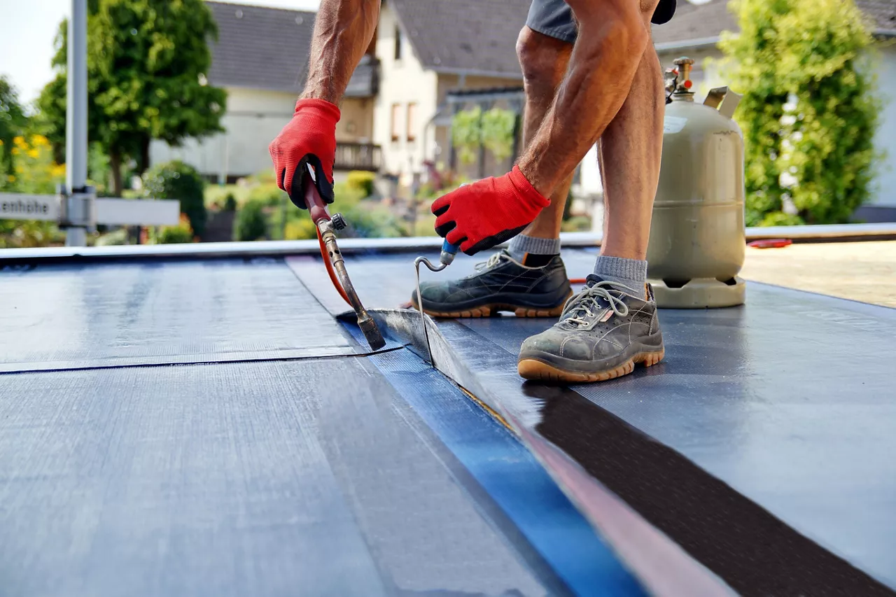 Flat roof installation with propane blowtorch during construction works with roofing felt. Heating and melting bitumen roofing felt. Roofing felt. Roofer working. Roofer working tool. Waterproofing