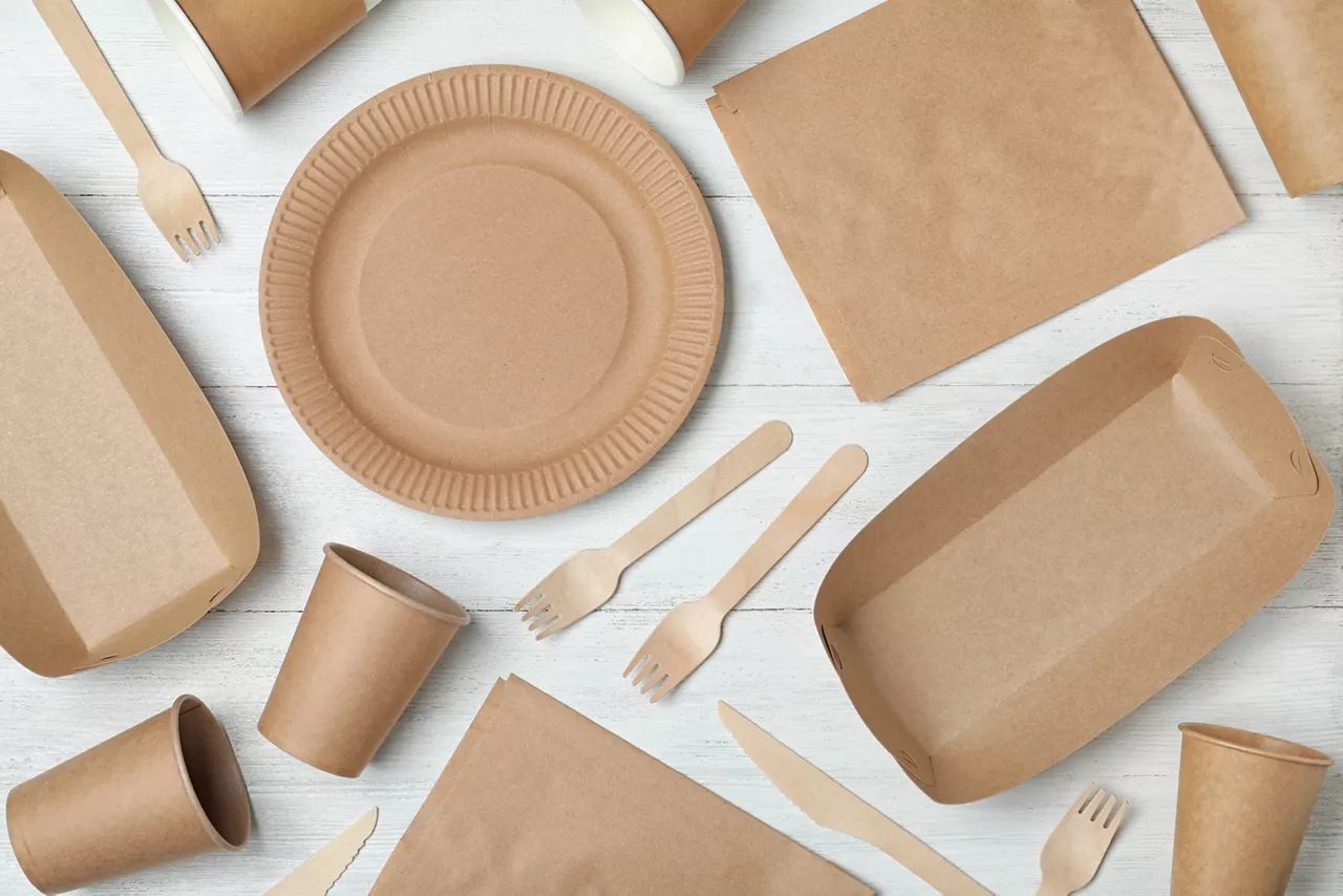 Paper utensils and packaging items on white wooden background