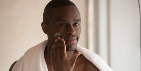 Young biracial man apply face cream after shower.