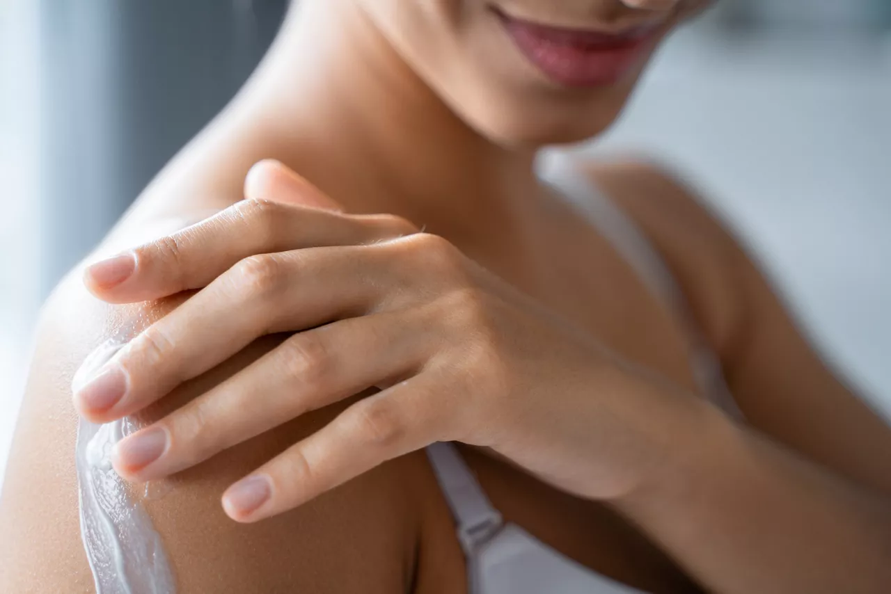 Cropped photo of a smiling young woman rubbing a body lotion into the arm