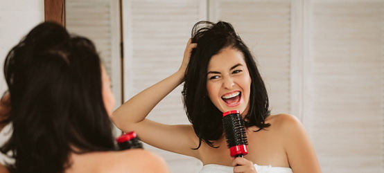 beautiful happy woman brushing healthy hair in front of the mirror. girl combing her hair and fools around