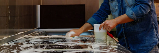 Employee cleaning and wipe out kitchen's cooking station on metallic or stainless steel surface with soap, mop and sponge.