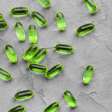 cápsulas transparentes de gelatina blanda verde colocadas sobre un fondo de hormigón gris 
