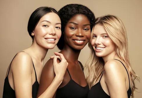 Diverse ethnicity women - Caucasian, African and Asian posing and smiling against beige background.