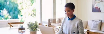 Young African American female entrepreneur using a laptop and writing notes while working from home