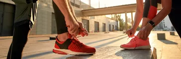 Two people in sport clothes tying shoelaces before running in sustainable footwear