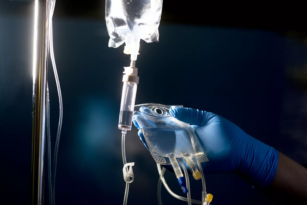 Nurse prepares secondary "piggyback" IV medication solution bag for administration with primary IV bag and IV tubing.