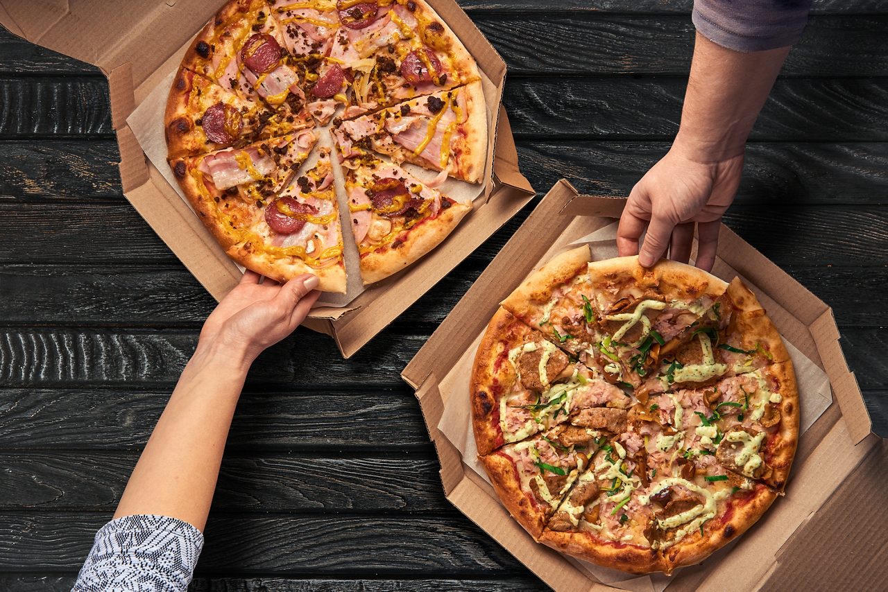 Manos tomando pizza de la caja de cartón