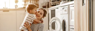 Happy family mother housewife and child son in laundry with washing machine