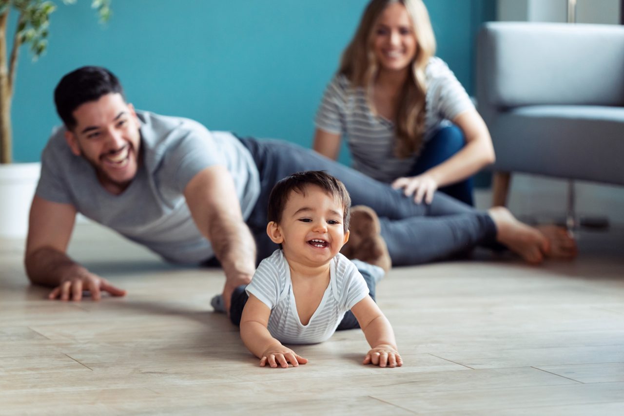 Pais brincando com o bebê sentados no chão em casa