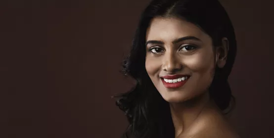 Portrait of young Indian woman with beautiful makeup and hairstyle on brown background.
