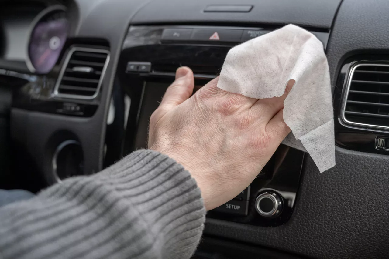 Man cleaning front dashboard of a car using wet wipe