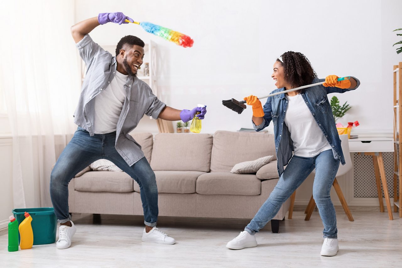Cheerful black couple playfully fighting with duster and swab