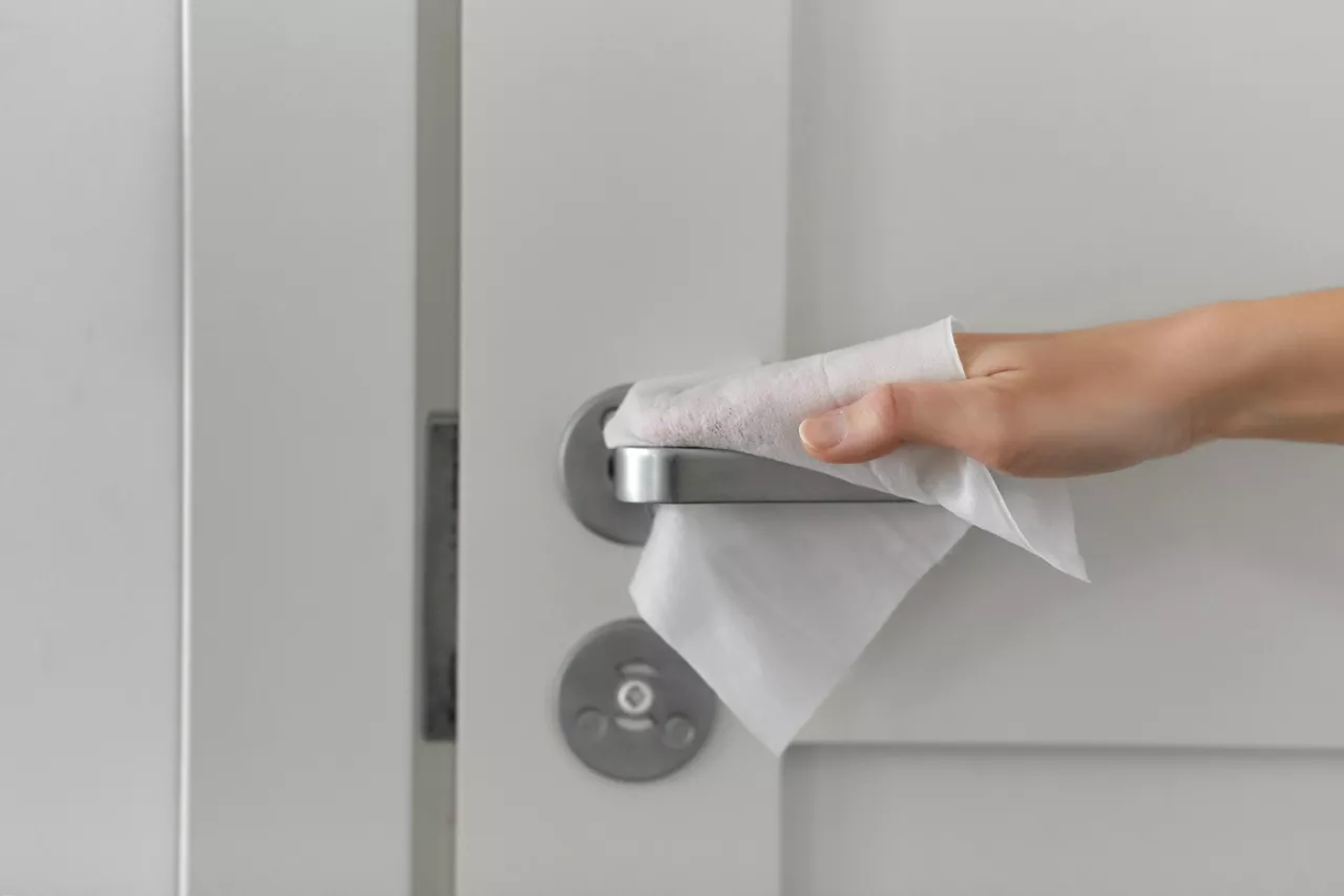 Close up of hand cleaning door handle surface with wet wipe