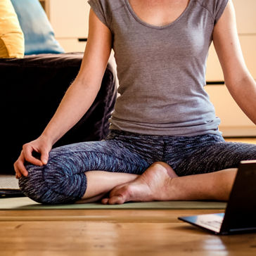 woman doing yoga on wood floor while watching videos on laptop
