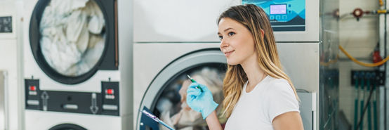 Female worker working with the laundry, she is operating with industrial washing machine.