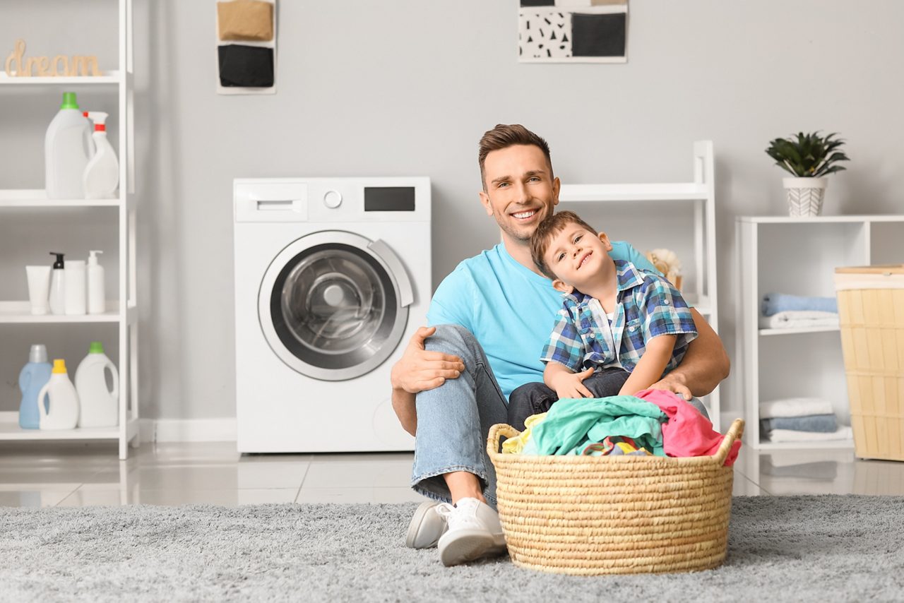 Pai e filho sentados no chão separando as roupas para lavar