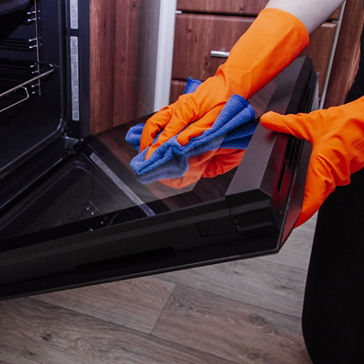 Women's hands in gloves with a microfiber cleaning cloth clean the oven door from the inside. Cleaning the kitchen concept