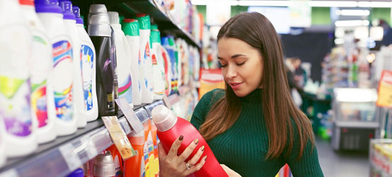 Joven ama de casa leyendo información sobre la botella de detergente en el supermercado.