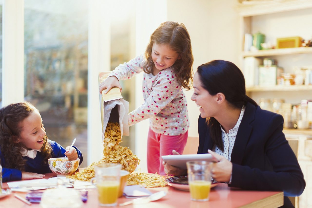 家族と朝食時にシリアルを箱から出して注ぐ少女。