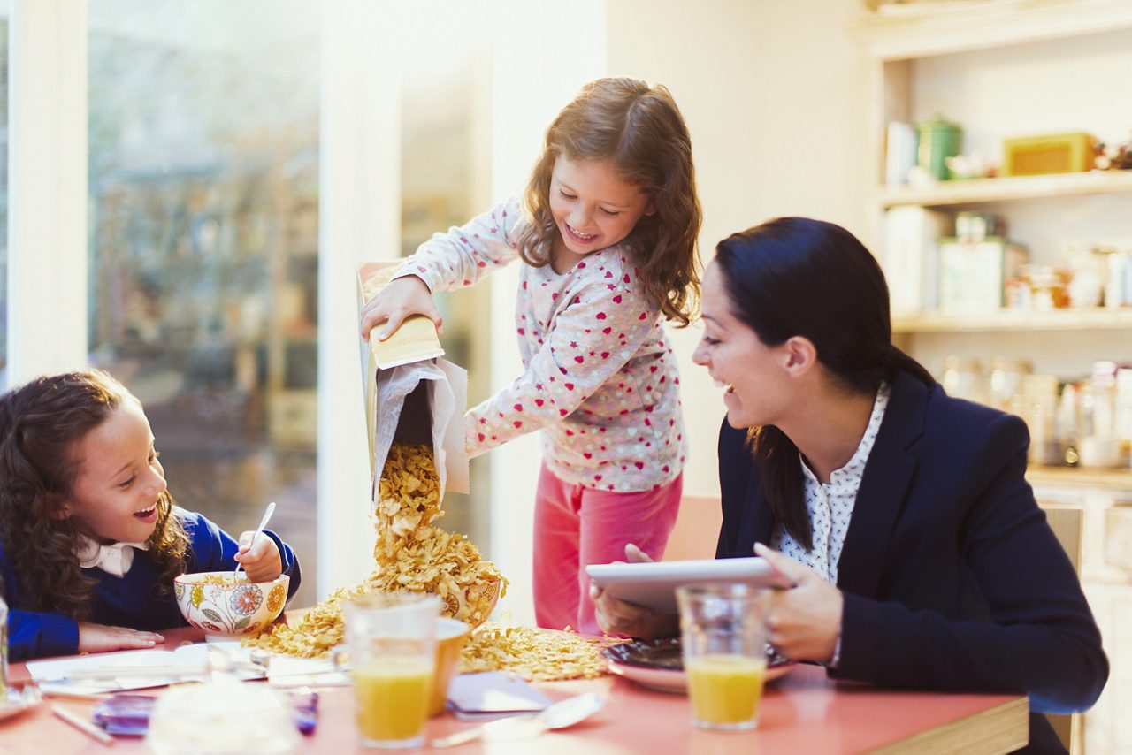 Girl pouring cereal out of box with at breakfast with family.