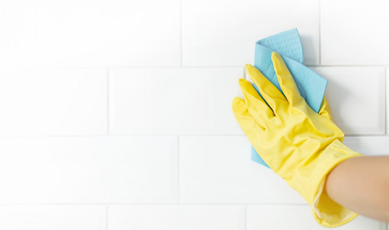 Mão com luva limpando os azulejos do banheiro